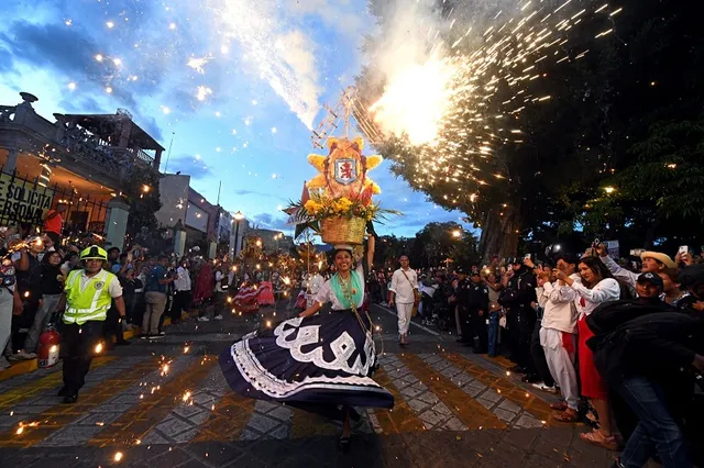 China oaxaqueña bailando con canasta de flores en una calenda nocturna con fuegos artificiales