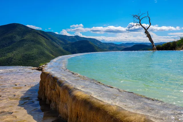 Poza turquesa al borde de la cascada petrificada de Hierve el Agua con montañas al fondo